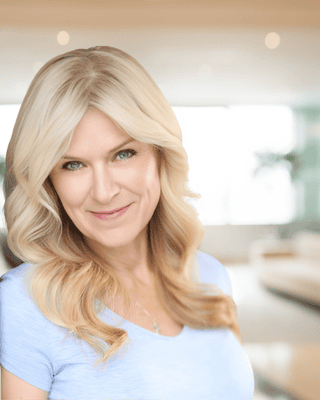 A woman with long blonde hair and a light blue shirt smiles at the camera in a bright, modern indoor setting, reflecting the positive impact of Foundation Funding.