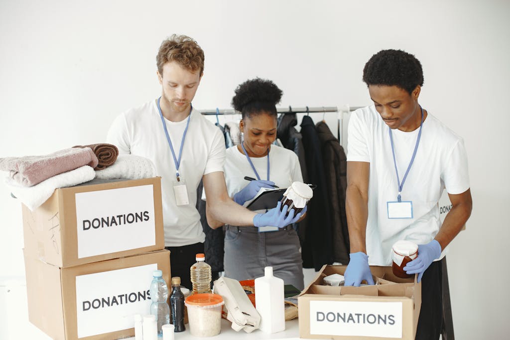 Three volunteers organizing donation boxes with clothes and food items in a community center.